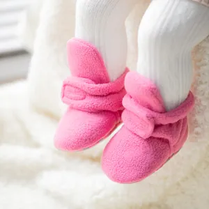 Primer plano de botines de forro polar rosa para bebé sobre un fondo blanco suave.