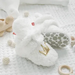 Detalle de cerca de los suaves zapatos de bebé en forro polar blanco con corona dorada