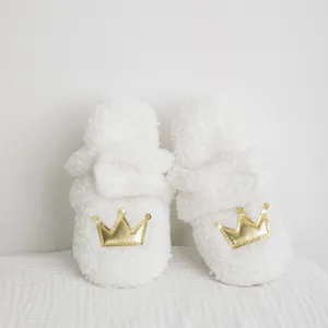 Vista detallada de patucos blancos de peluche para bebé con bordado de corona dorada