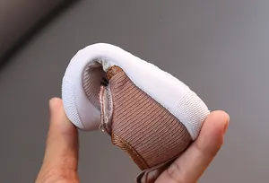 Close-up view of a flexible brown baby toddler shoe being bent to demonstrate the soft sole