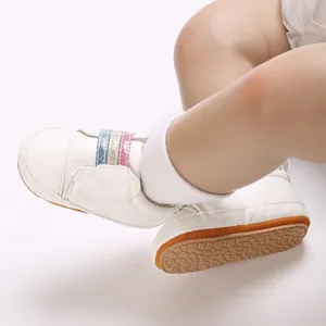 Detailopname van witte babyschoenen met regenboogbandjes en zachte antislipzolen