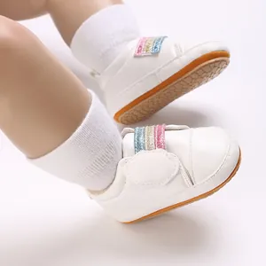 Detailopname van witte babyschoenen met regenboog glitterbandjes en zachte zolen.
