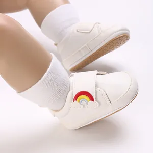 Gedetailleerd overzicht van witte babyschoentjes met regenboogborduurwerk en zachte zool