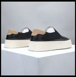 Rear view of black leather platform loafers with beige heel patch on white cube.