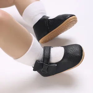 Macro view of black faux leather baby Mary Janes with soft soles and a bow detail.