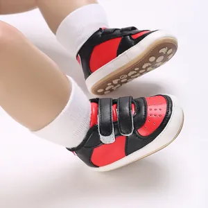 Baskets de sport pour bébé bicolores rouge et noir présentées sur pieds de poupée
