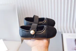 Primer plano de zapatos Mary Jane negros para niña con botón de perla y punta de ante