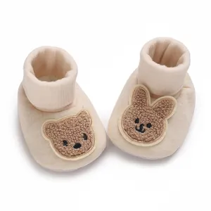 Vue détaillée de chaussons en coton beige pour bébé avec ours et lapin brodés.