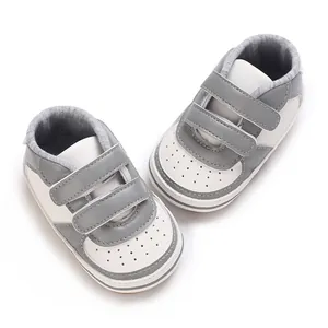 Vue de dessus de baskets bébé bicolores gris et blanc avec fermetures à scratch.