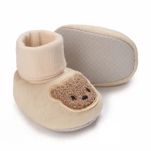 Gros plan détaillé de bottines bébé beige avec semelle antidérapante et motif ours.