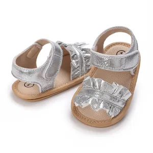 Close-up of silver baby girl sandals featuring ruffled details and soft soles for toddlers.