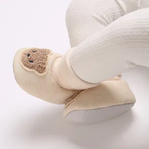 Vue détaillée de chaussons bébé beiges avec un écusson ours en peluche tout doux