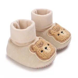 Gros plan sur des chaussons bébé beiges avec une broderie d'ours en peluche adorable