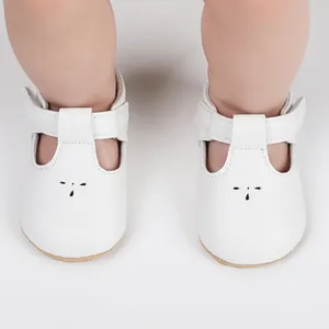 Close-up of white faux leather baby walking shoes with T-strap design worn by an infant
