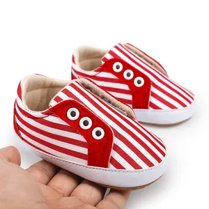 Gros plan de chaussures de marche pour bébé à rayures rouges et blanches tenues à la main.