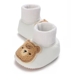 Gros plan de chaussons pour bébé blancs avec un joli motif d'ours en peluche brodé.
