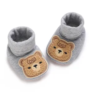 Détail de chaussons tricotés gris pour bébé avec un joli patch d'ours en peluche