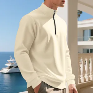 Vista laterale di una felpa da uomo crema con mezza zip su uno sfondo costiero di mare