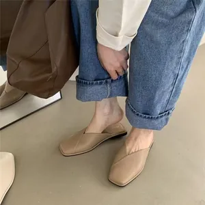 Close-up showing the fit of beige flat square toe mules worn with stylish blue denim jeans
