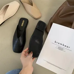 Detail view of black and beige square toe flat mules showing the textured rubber sole.