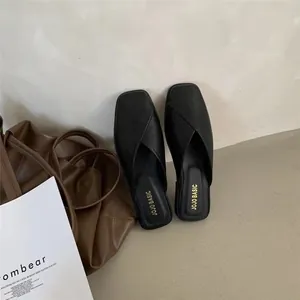 Detailed top-view of black square-toe flat mule slippers beside a brown fashion tote bag