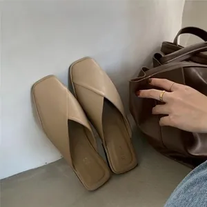 Detail view of stylish beige square-toe mules featuring a soft leather cross-over design