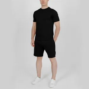 Full body view of a man wearing a plain black t-shirt and shorts set in a studio setting