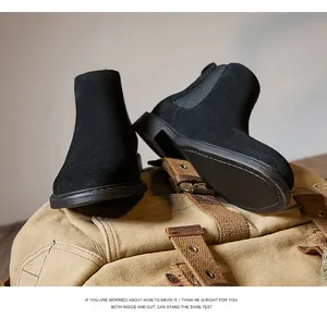 Close-up of black suede Chelsea boots on a tan canvas backpack in a rustic setting