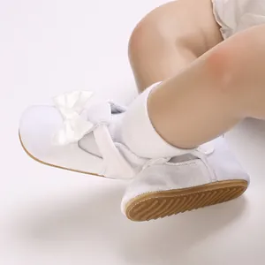 Detailed view of white infant walking shoes featuring a delicate ribbon bow and anti-slip sole