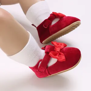 Close-up of red velvet baby walking shoes with ribbon bows and soft soles for infants.