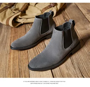 Premium grey suede men's Chelsea boots displayed on a rustic wooden floor with a backpack