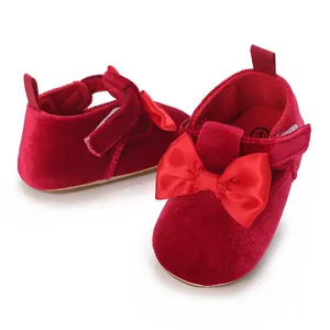 Close-up detail of red velvet baby walking shoes featuring a satin bow and velcro strap