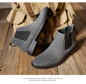 Close-up of grey suede Chelsea boots paired with a vintage canvas backpack on wood.