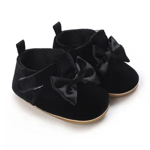 Close-up detail of black velvet infant walking shoes featuring elegant satin bows
