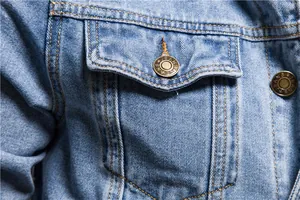 Detailed macro shot of the chest pocket and engraved metal button on a blue denim jacket