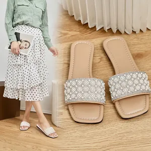 Women's square-toe flat sandals with pearl and rhinestone embellishments on wood floor.