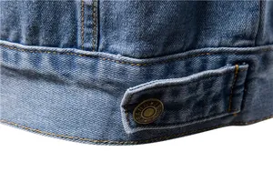 Close-up macro detail of blue denim jacket hem showing yellow stitching and metal button