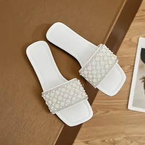 Close-up detail of white square-toe slippers with elegant pearl and rhinestone flower patterns
