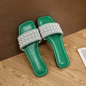 Close-up detail of stylish green square-toe flat slides with elegant pearl beaded straps
