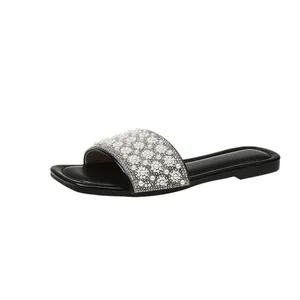 Detailed side view of women's black flat slide sandals with pearl and rhinestone embellishment