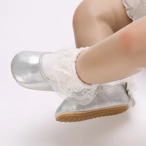 Detailed close-up of silver glitter baby shoes with white lace ruffle socks on white background