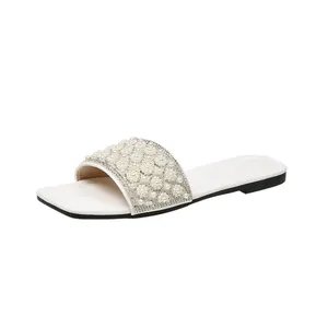 Detail view of white square toe flat slides with pearl and rhinestone floral design.