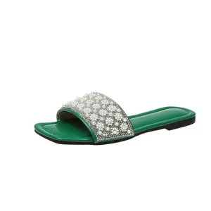 Detail view of green flat slide sandal with pearl and rhinestone flower strap.