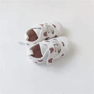 Top-down detail of soft-soled white children's canvas shoes with cute bear pattern
