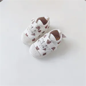 Close-up of white toddler canvas shoes featuring a cute brown bear pattern and soft rubber soles.