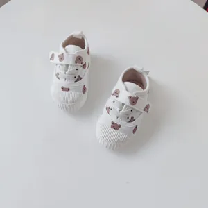 A top view of white baby canvas sneakers featuring cute brown bear prints and soft rubber soles