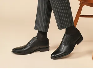 Gros plan de chaussures Oxford en cuir noir portées avec un pantalon de costume à rayures