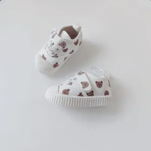 Detailed view of white baby canvas shoes with a cute brown bear pattern and soft rubber soles.