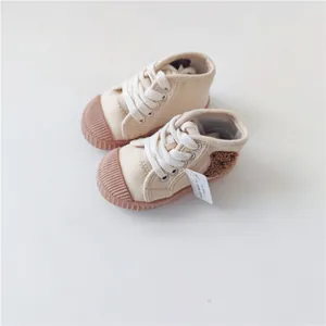 Close-up of beige baby canvas shoes with a cute plush bear patch and white laces