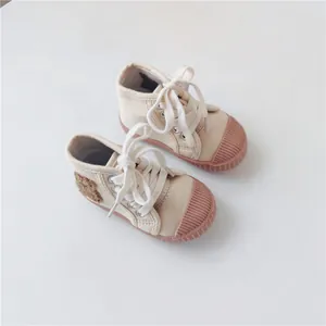 Close-up of beige children's high-top canvas shoes with cute bear patch and pinkish rubber soles